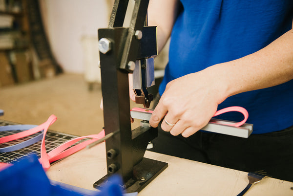 woman in blue shirt standing in front of a rivet machine holding pink biothane