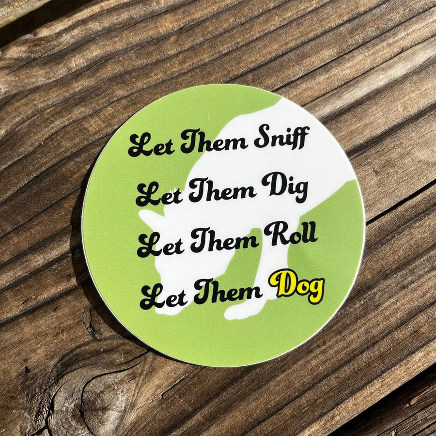 green round sticker with white shadow of a dag and the words that say: Let Them Sniff, Let Them Deg, Let Them Roll, Let Them Dog on a wood background