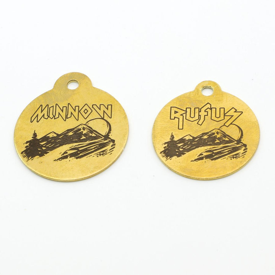 two brass Dog ID Tags with the mountain scene and then names Minnow and Rufus