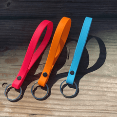 three biothane key fobs  on a wood table in red, orange, and light blue