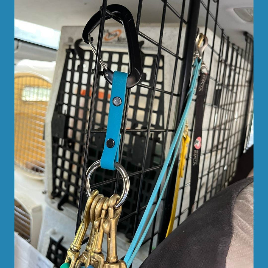 close up of a dog crate with the teal mini leash organizer hanging on the side with several brass hardware leashes attached