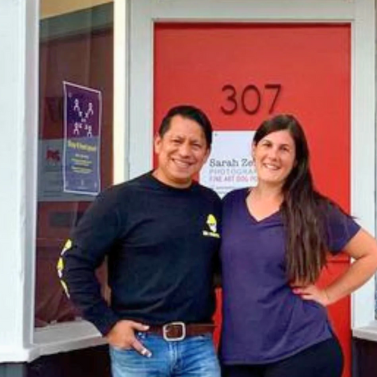 man wearing a black shirt and jeans next to a woman in a purple shirt and black pants standing in front of a red door with the numbers 307