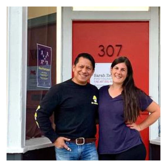 man wearing a black shirt and jeans next to a woman in a purple shirt and black pants standing in front of a red door with the numbers 307
