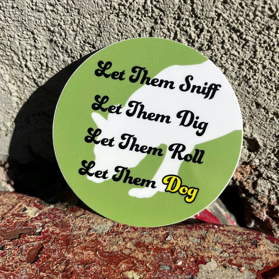 green round sticker with white shadow of a dag and the words that say: Let Them Sniff, Let Them Deg, Let Them Roll, Let Them Dog on a brick background