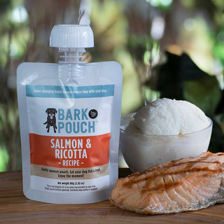 White, Blue, and orange Bark Pouch dog treat in Salmon & ricotta recipe on a table with a piece of salmon and a bowl of ricotta