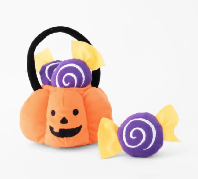 plush orange pumpkin basket with black handle and three purple and yellow pieces of candy for dog burrowing