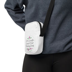 close up of person wearing white crossbody bag that reads in cross stitch font "Live, Laugh, Leash your F-ing Dog