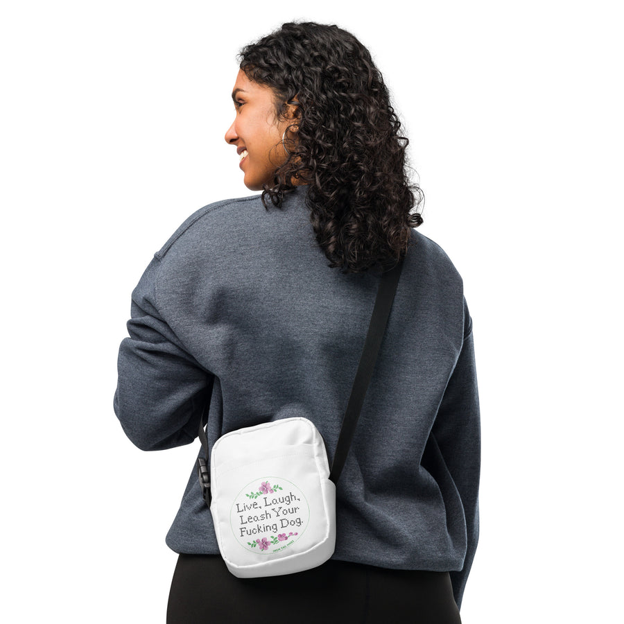 person wearing white crossbody bag that reads in cross stitch font "Live, Laugh, Leash your F-ing Dog