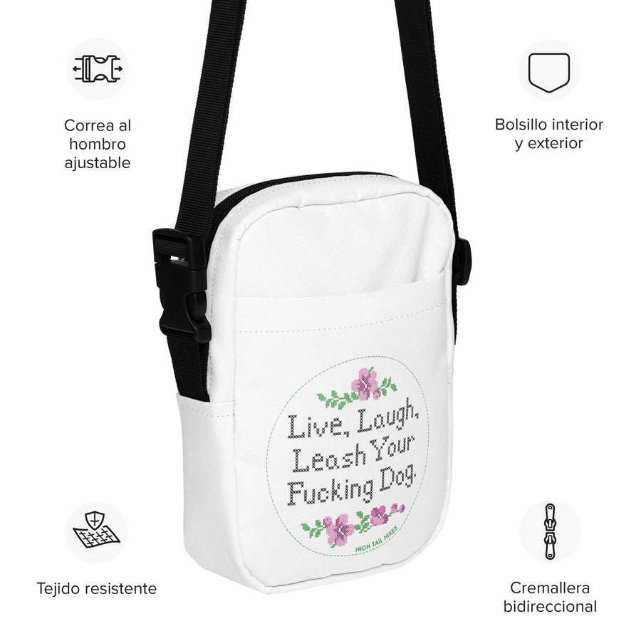 white crossbody bag that reads in cross stitch font "Live, Laugh, Leash your F-ing Dog with product details in spanish