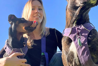 Alyssa Soares with two dogs wearing purple harnesses against a clear blue sky.