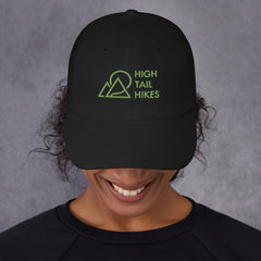 woman wearing black dad hat with green high tail hikes logo with her head tilted down to show the hat