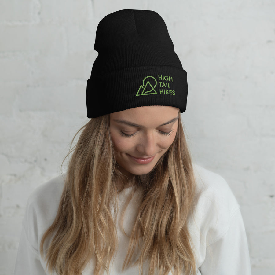 woman tilting her head down, wearing black cuffed beanie with green high tail hikes logo