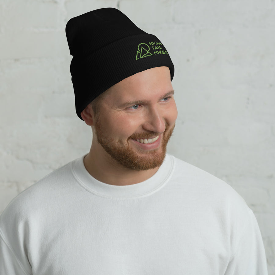 man smiling, wearing a white sweatshirt and black cuffed beanie with green high tail hikes logo