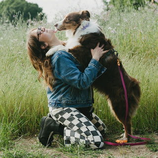 Woman hugging a dog that is wearing a waterproof leash in a field of tall grass