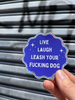 hand holding silver and blue sticker that says "Live Laugh Leash your $ucking dog