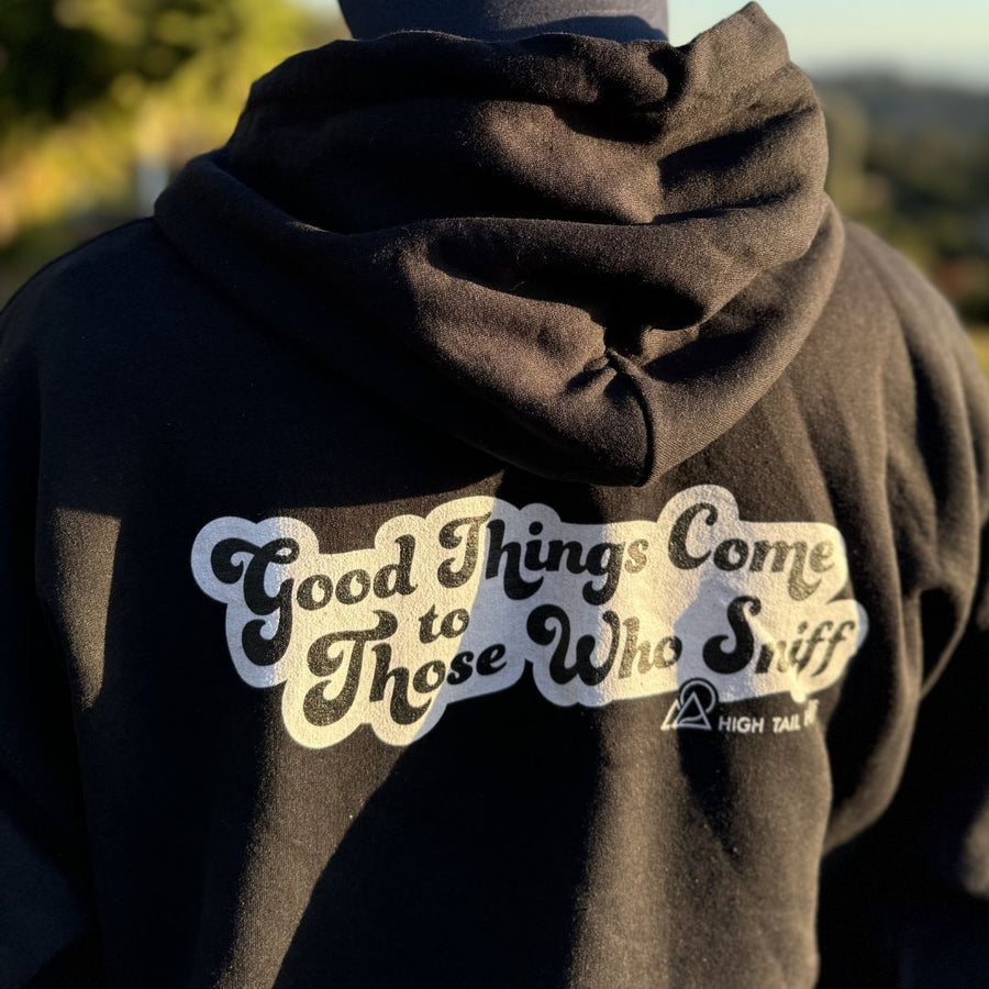 Person standing outside facing away from camera, showing the back of black hoodie that reads "good Things Come to Those Who Sniff" with the white High Tail Hikes logo underneath in white
