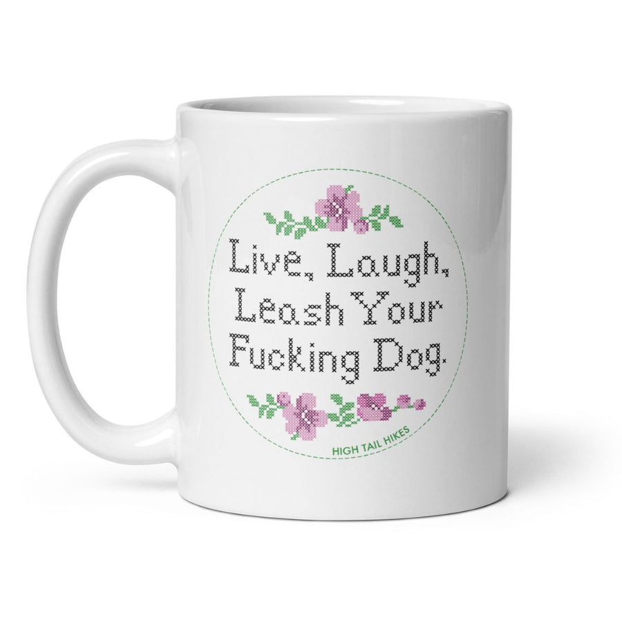 white ceramic mug, handle to the left, reads "Live, Laugh, Leash Your F Dog" in cross stitch font