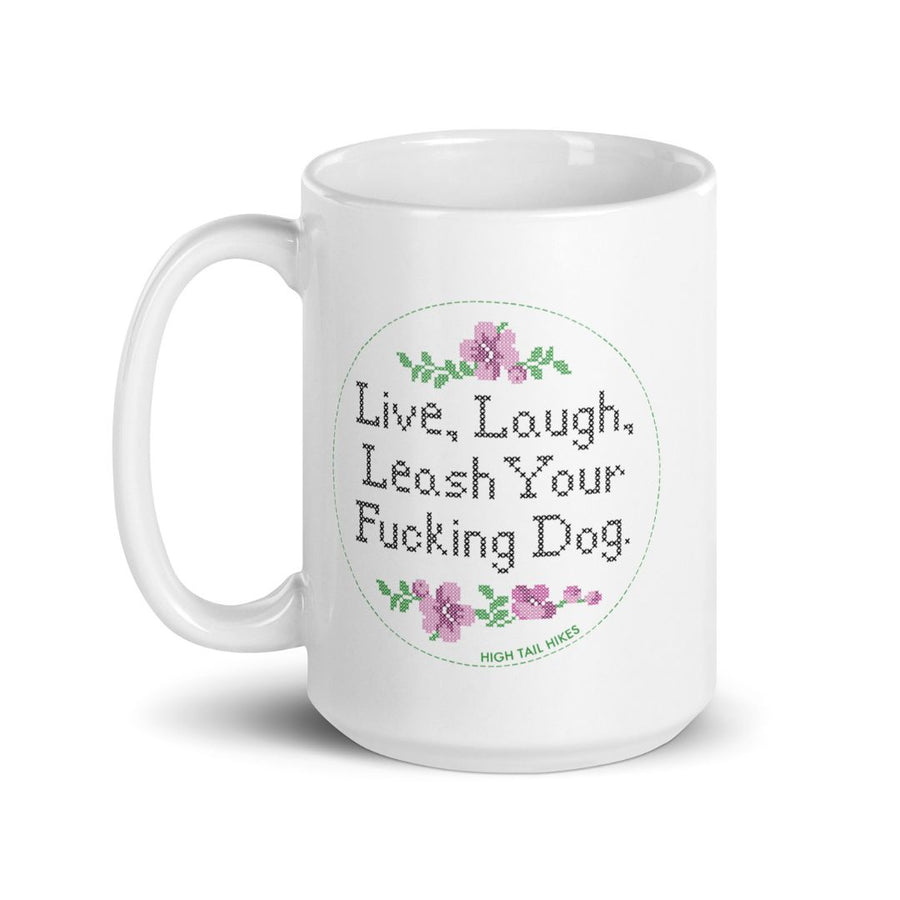 white ceramic mug, handle to the left, reads "Live, Laugh, Leash Your F Dog" in cross stitch font