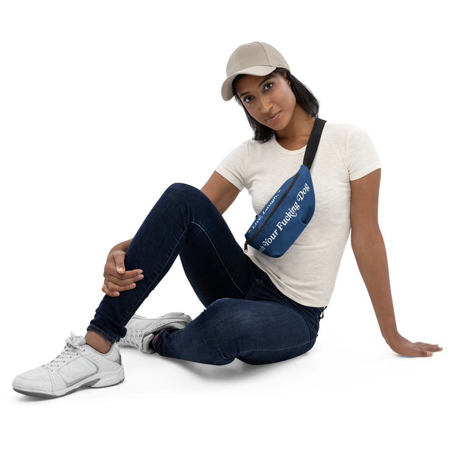 woman sitting, wearing white tennis shoes, jeans, white t-shirt, white hat, and across her chest is a blue fanny pack that reads "Live Laugh, Leash your F Dog"