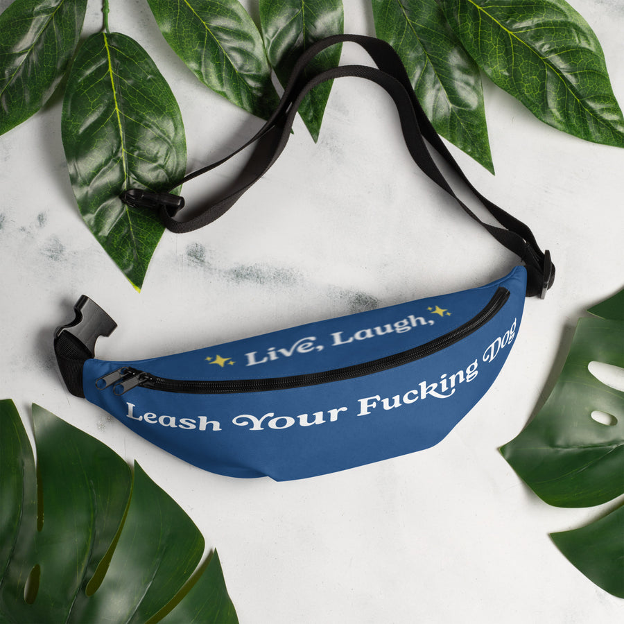 blue fanny pack on white back ground with large green leaves  - the blue fanny pack has white letters that read "Live, Laugh, Leash Your F Dog"