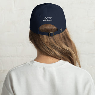 back of womans head, she is wearing a white sweater, and dark blue dad hat with white high tail hikes logo above the adjustable strap