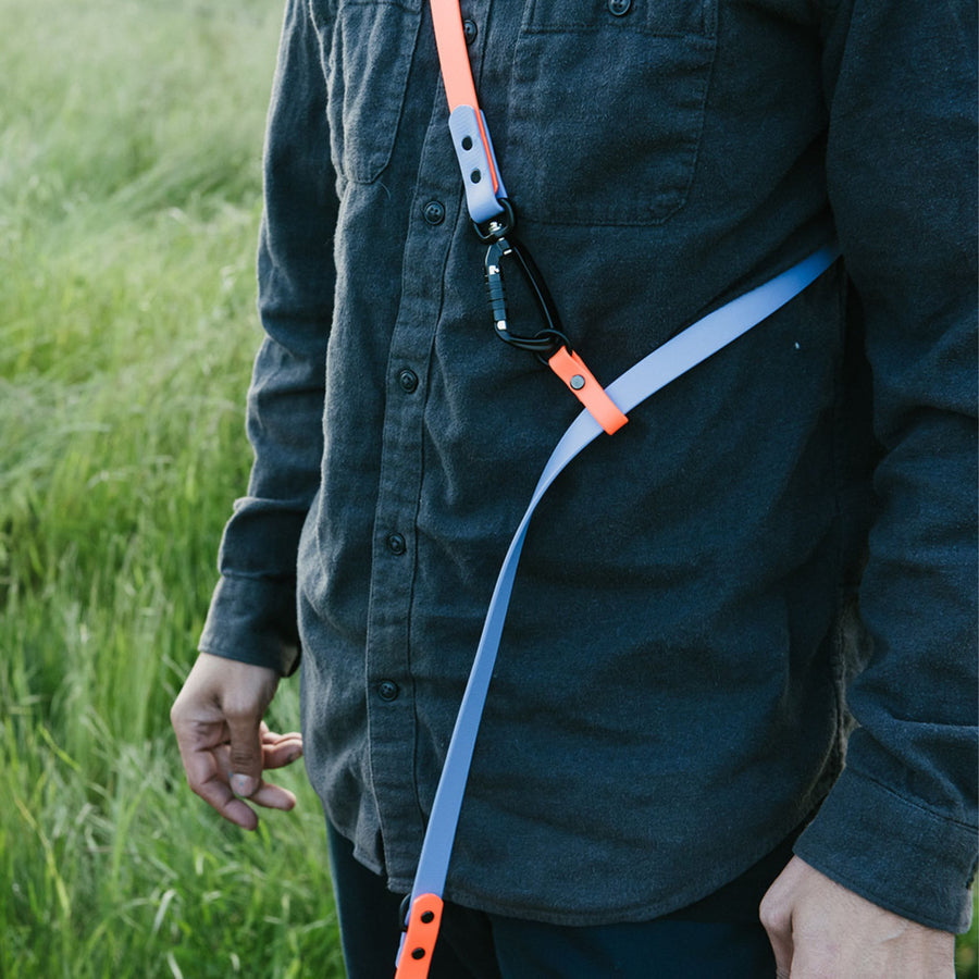Person wearing a dark shirt with a blue and orange hands-free leash attached, standing in a grassy field.