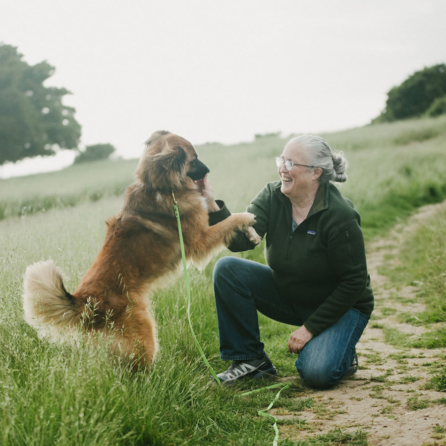 Woman kneeling on a grassy path with a brown dog wearing a waterproof leash, both looking happy
