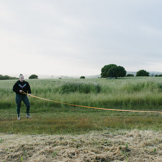 Person holding a long waterproof leash in a grassy field with trees in the background