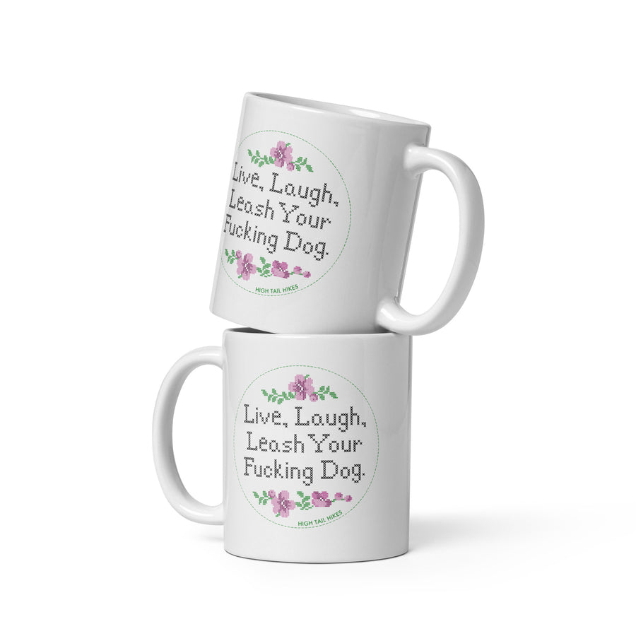 two white 11 oz ceramic mugs stacked, both read "Live, Laugh, Leash Your F Dog" in cross stitch font