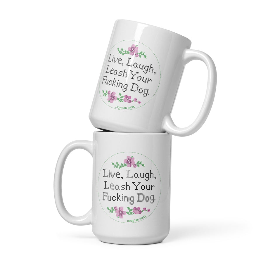 two white 15 oz ceramic mugs stacked, both read "Live, Laugh, Leash Your F Dog" in cross stitch font