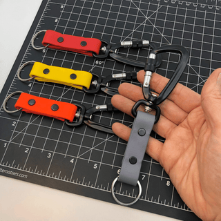 hand holding one sport biothane keychain over a black ruler mat and three sport biothane keychains