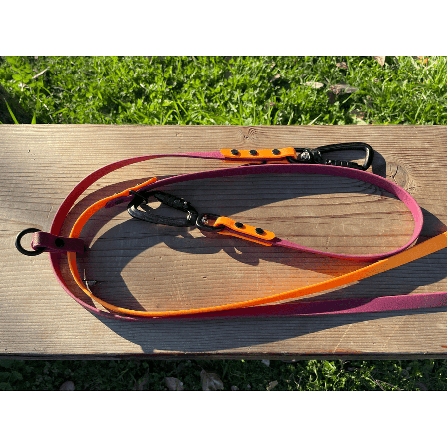 biothane dog leash in orange and pink laying on bench with grass in the background with sport hardware