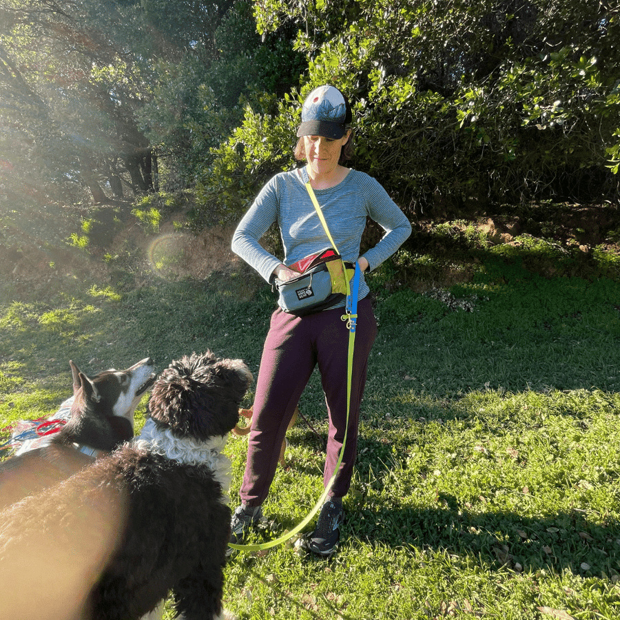 women wearing fanny pack near trees with two dogs in front of her waiting on a treat wearing biothane dog leash
