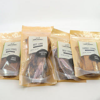 four packages of farm hounds treats laying on a table in tan package w/ clear front