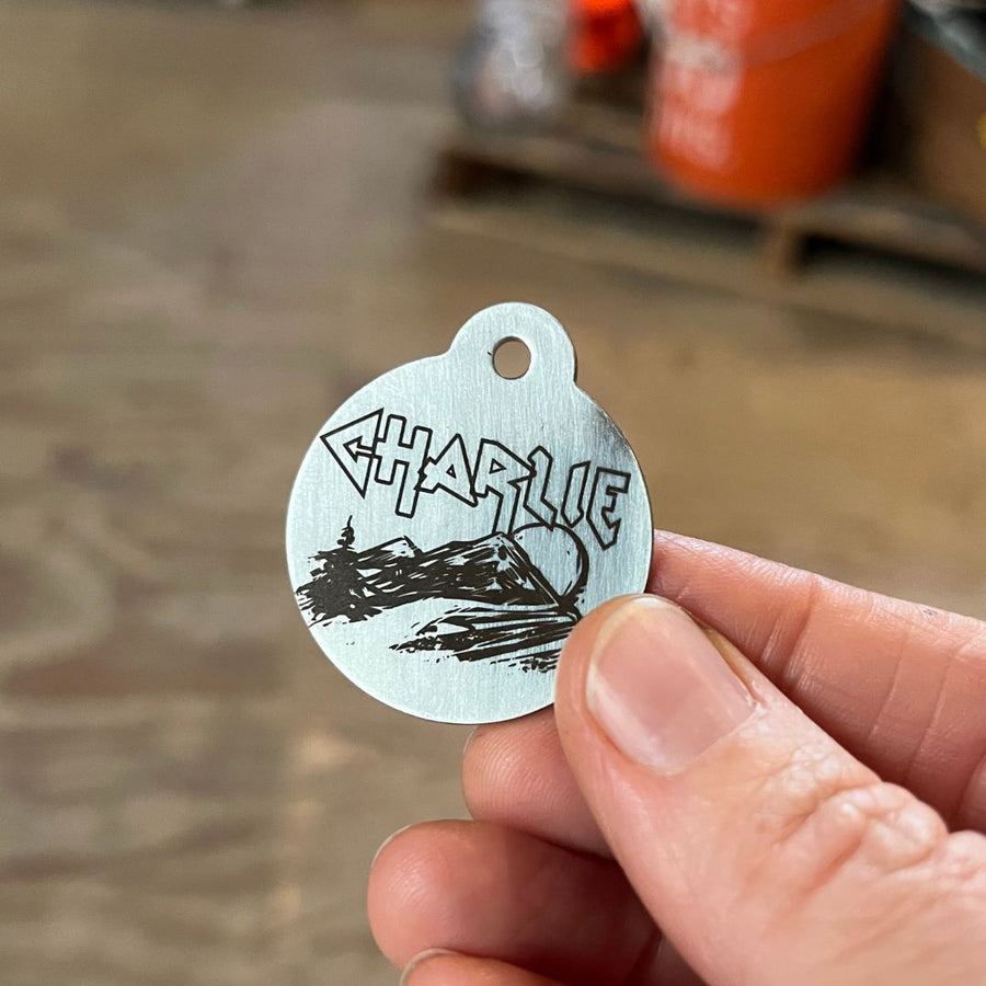 hand holding a silver mountain metal graphic ID dog tag with the name Charlie