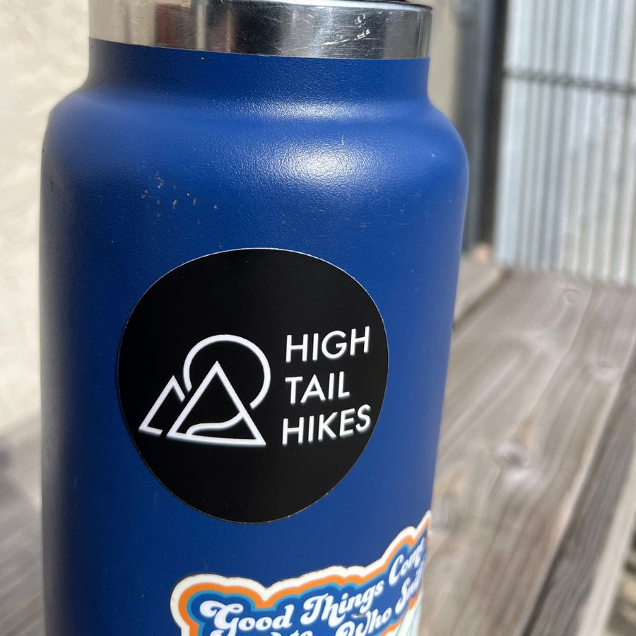 round black sticker with white High Tail Hikes logo on a blue water bottle