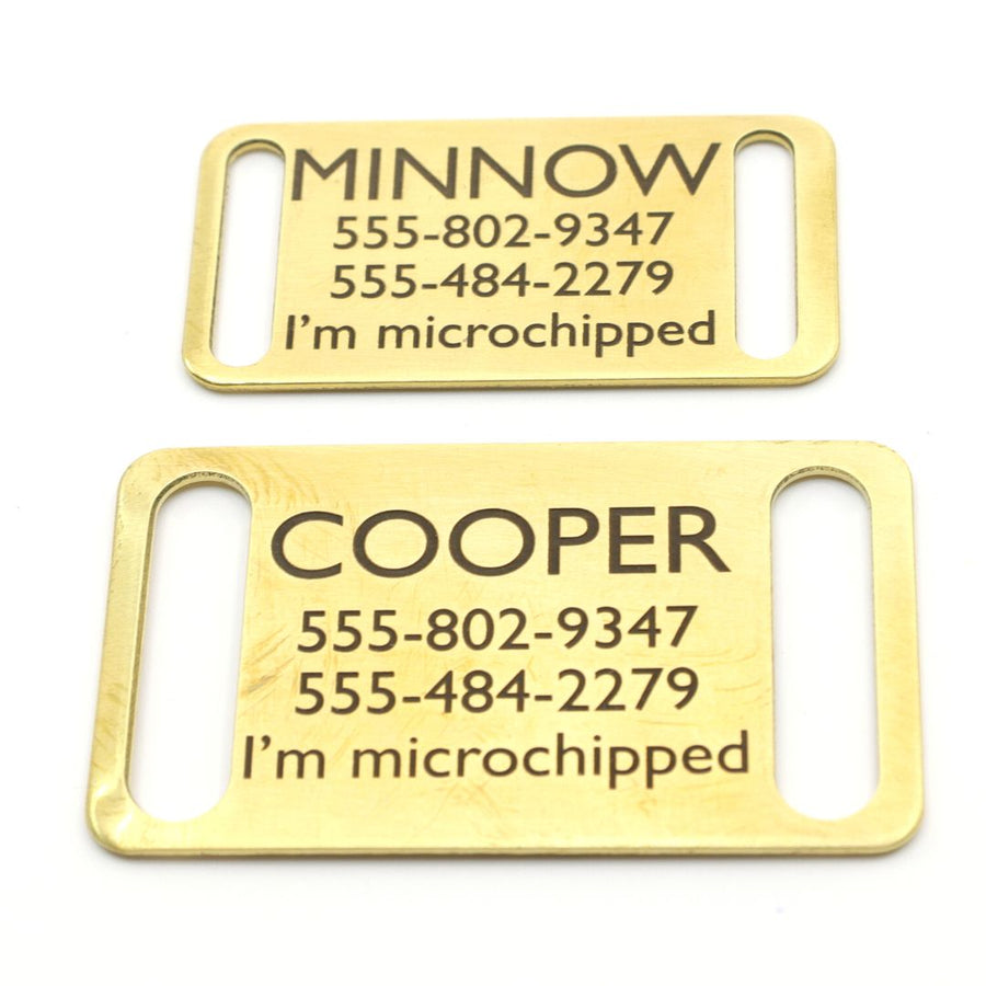 close up of two brass slide on dog ID tags in brass with the pets name, 2 phone numbers and note "I'm microchipped"