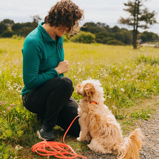 women next to small tan dog that is wearing an orange biothane dog leash