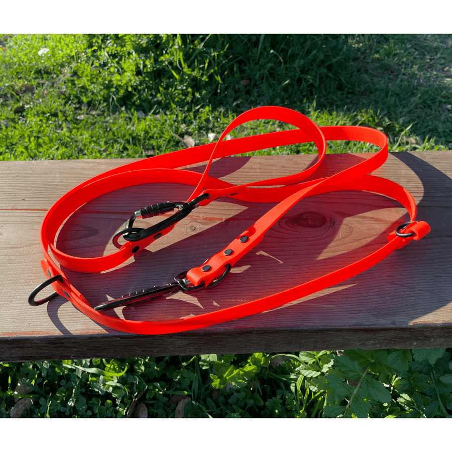 red biothane dog leash folded on bench near grass wtih sport hardware