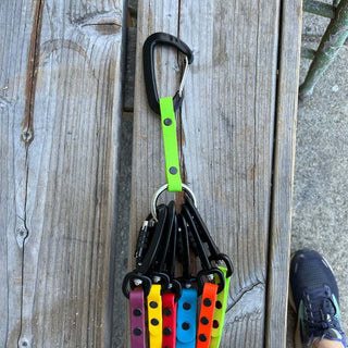 Green Apple Biothane Mini Leash Organizer laying on a bench with several sport leashes attached