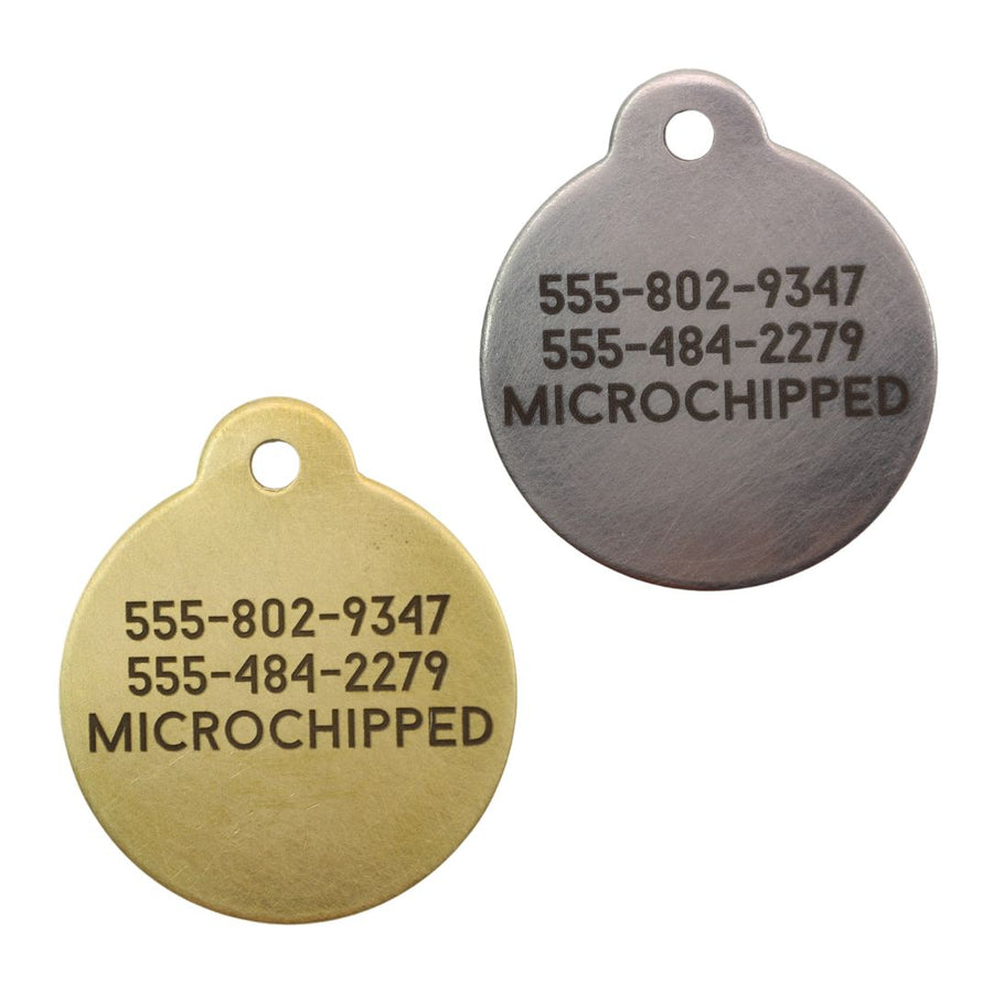 the back of a silver and a brass mountain metal graphic ID dog tag showing the owners phone number and the note "microchipped"