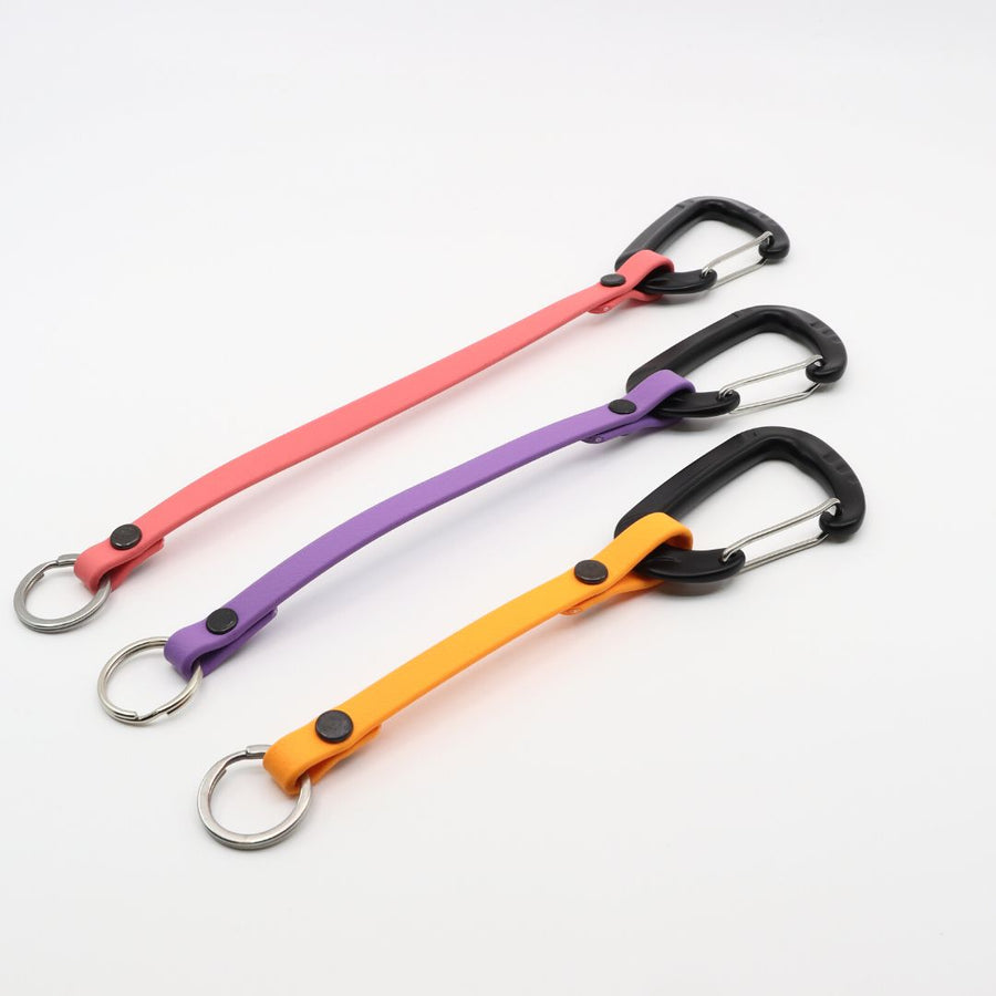 three lengths of biothane clicker straps with carabiner clip on a white background in flamingo, lavender, and golden rod colors