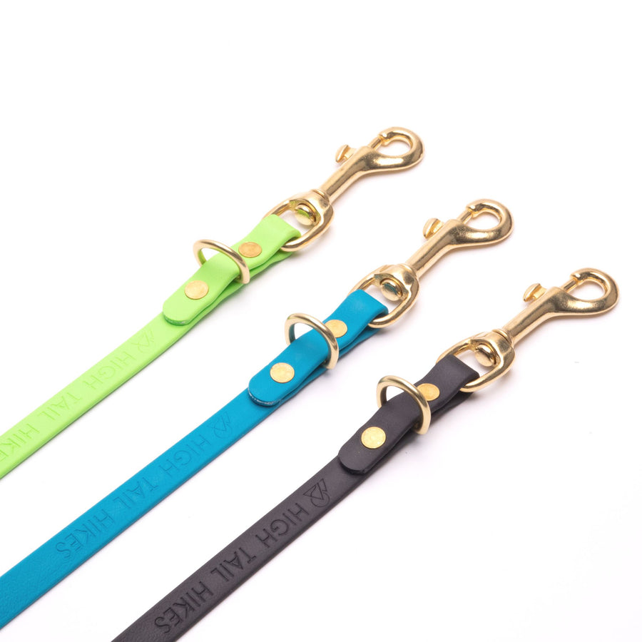 green, blue, and black biothane hands free leash with brass hardware close up on white background
